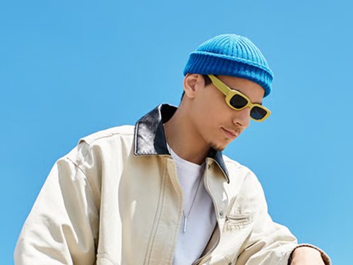 Jovem de boné azul e óculos escuros sobre fundo de céu azul